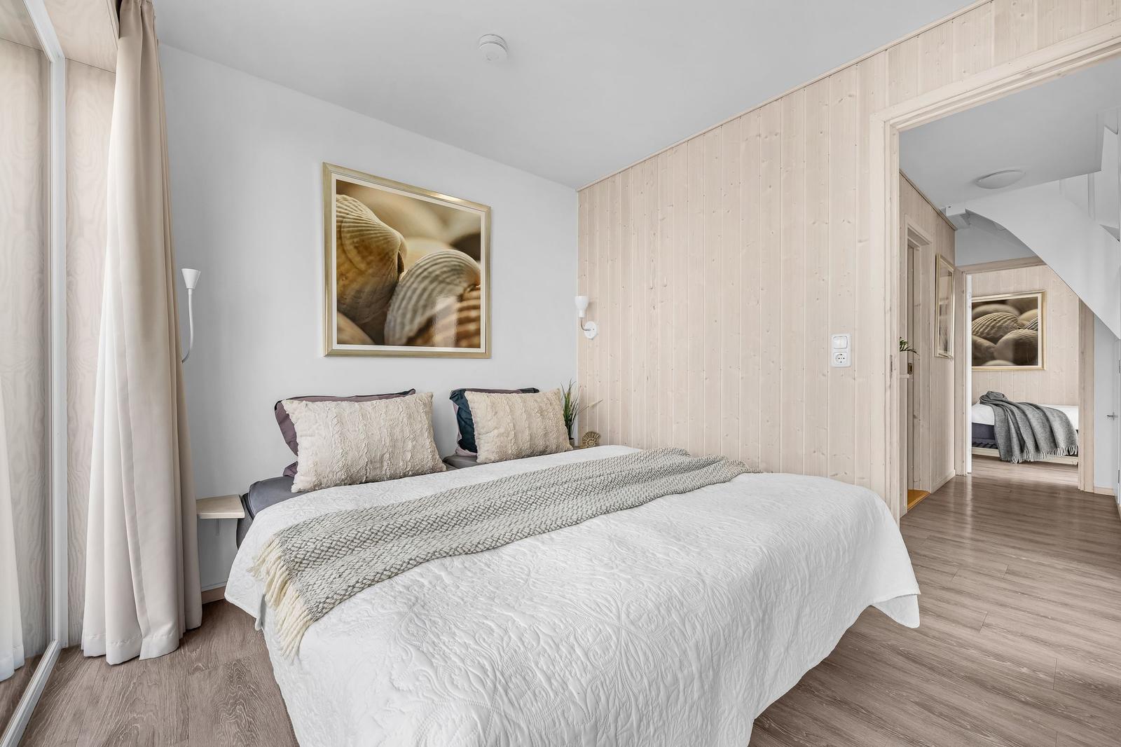 Schlafzimmer mit Bett, Wandbild und Holzwand. Durchgang zu einem weiteren Raum.