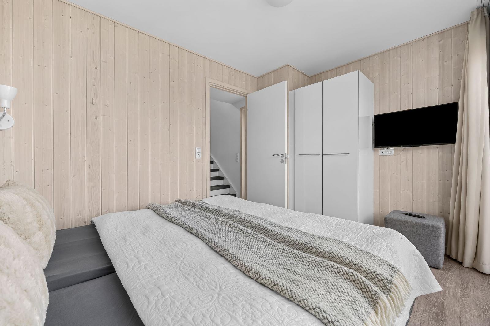 Schlafzimmer mit Bett, Kleiderschrank und Fernseher an der Wand.