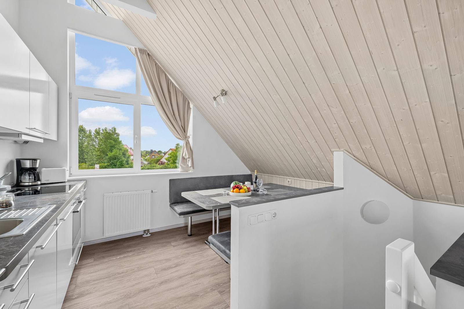 Küche mit Essbereich unter Dachschrägen, großes Fenster mit Blick auf Grün.