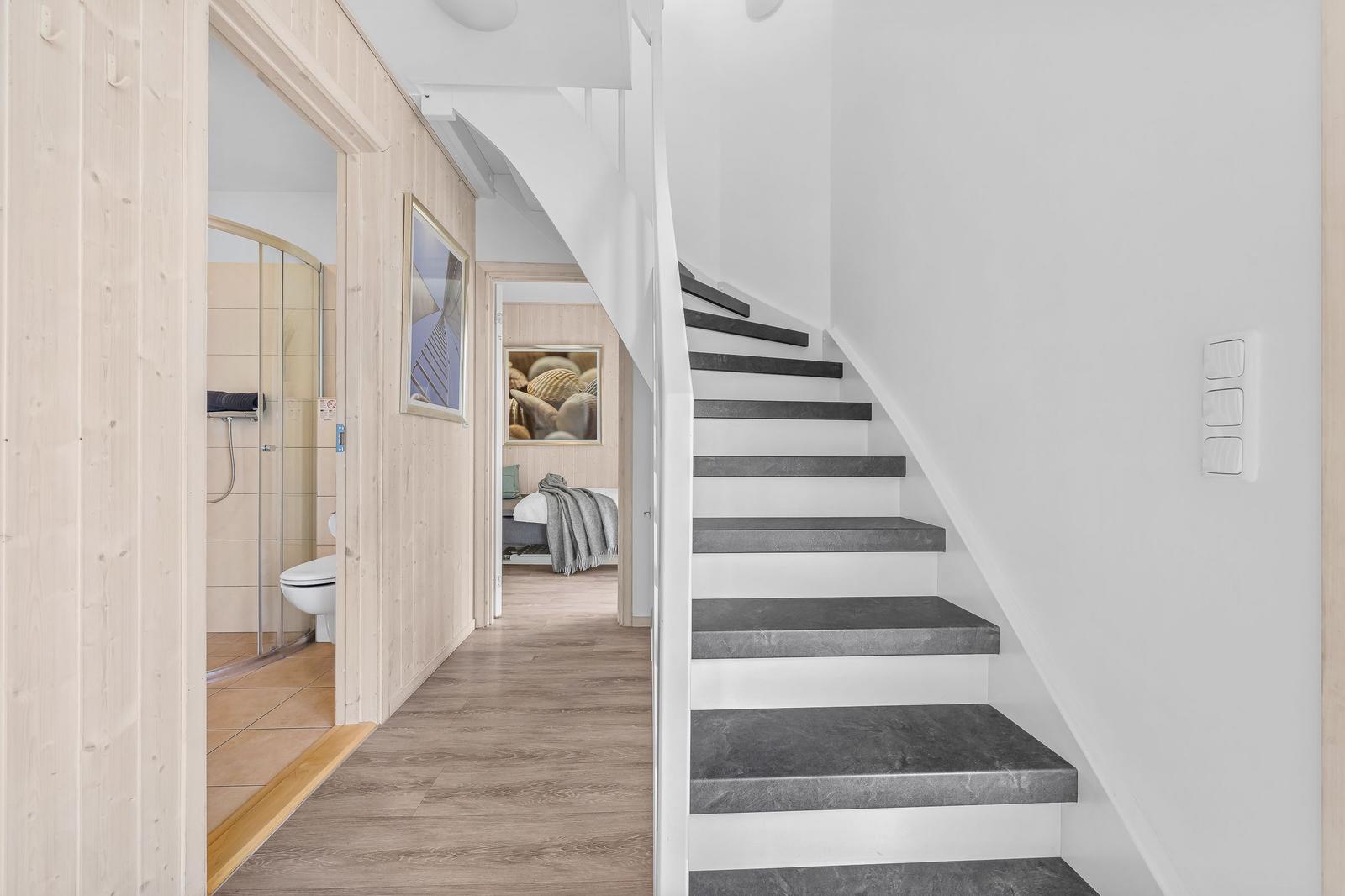 Treppenhaus mit grauen Stufen, angrenzende Bade- und Schlafzimmer.