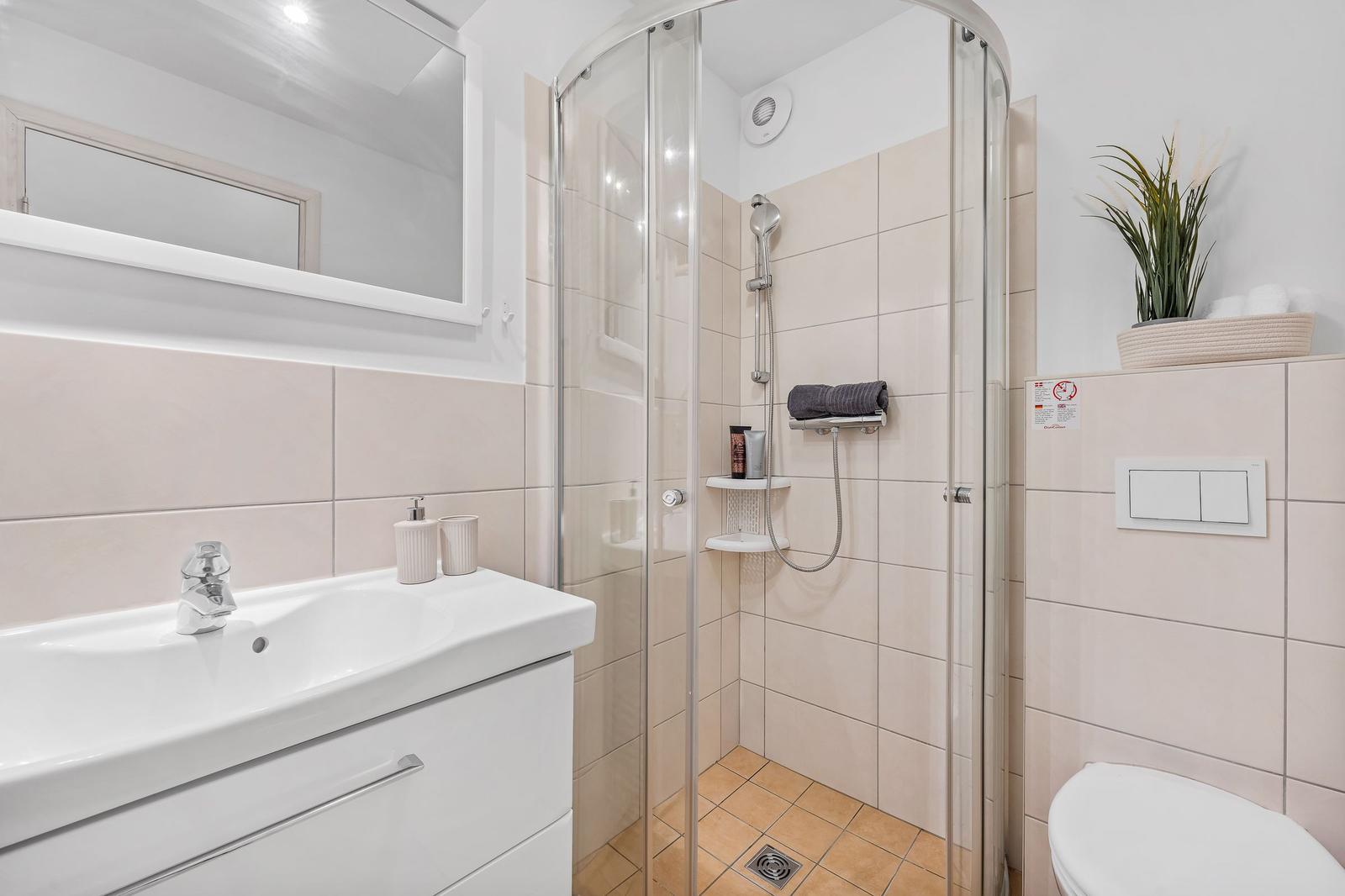 Badezimmer mit Dusche, Waschbecken und Toilette. Fliesenwand und Spiegel.
