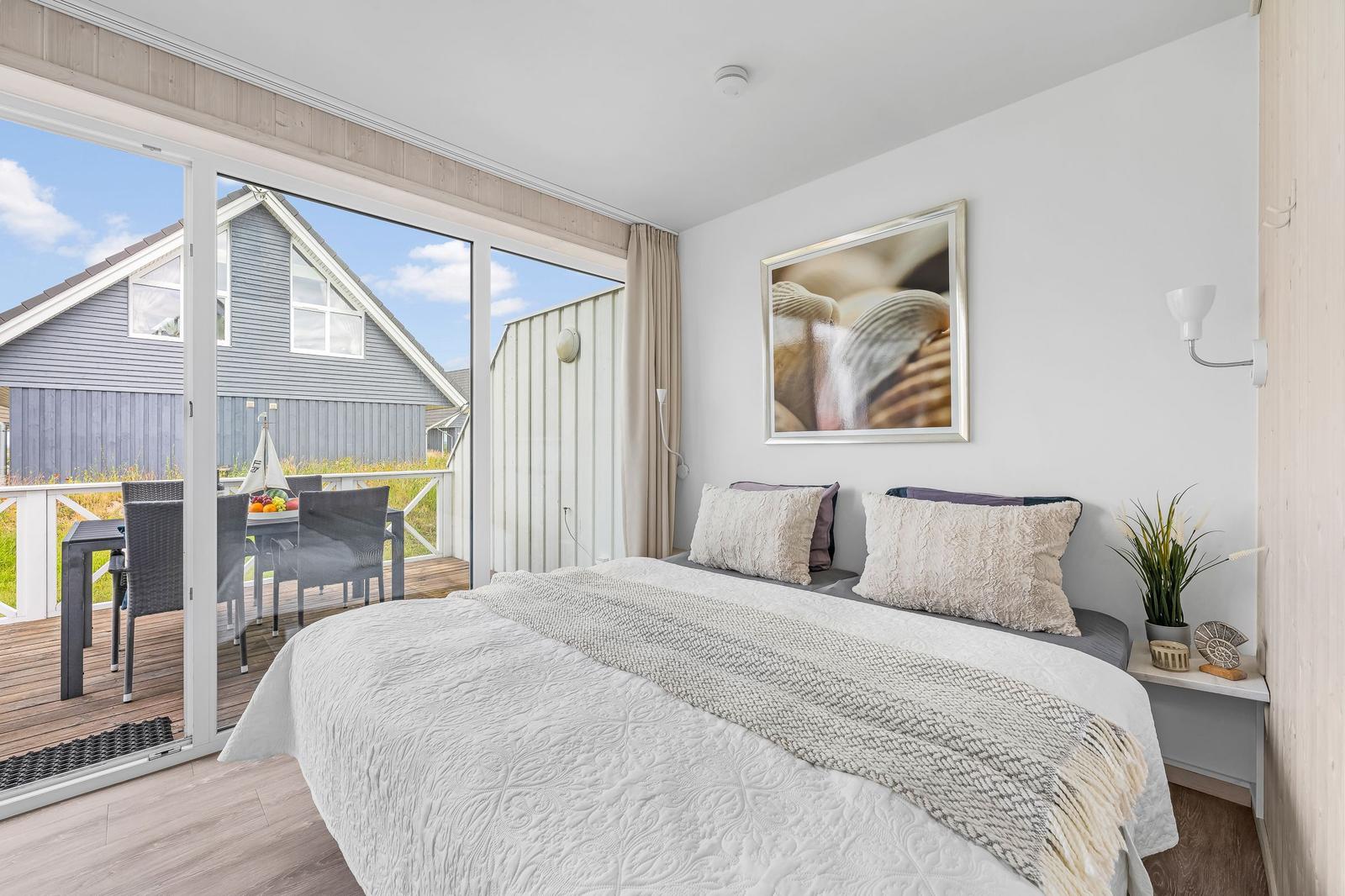 Schlafzimmer mit Balkon, Bett, Wandbild und Pflanze.
