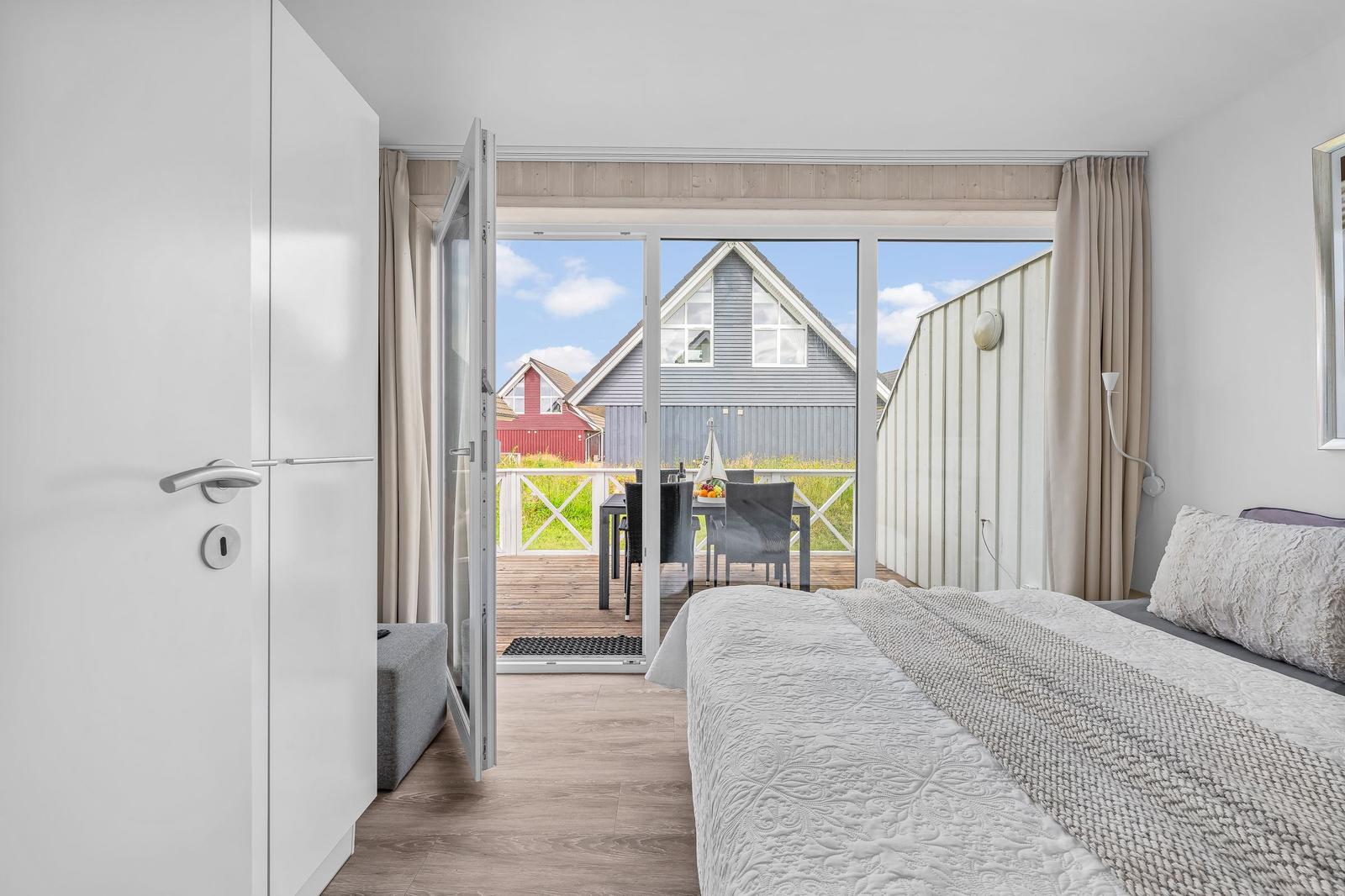 Schlafzimmer mit Balkonblick auf Holzhäuser und Grünflächen.