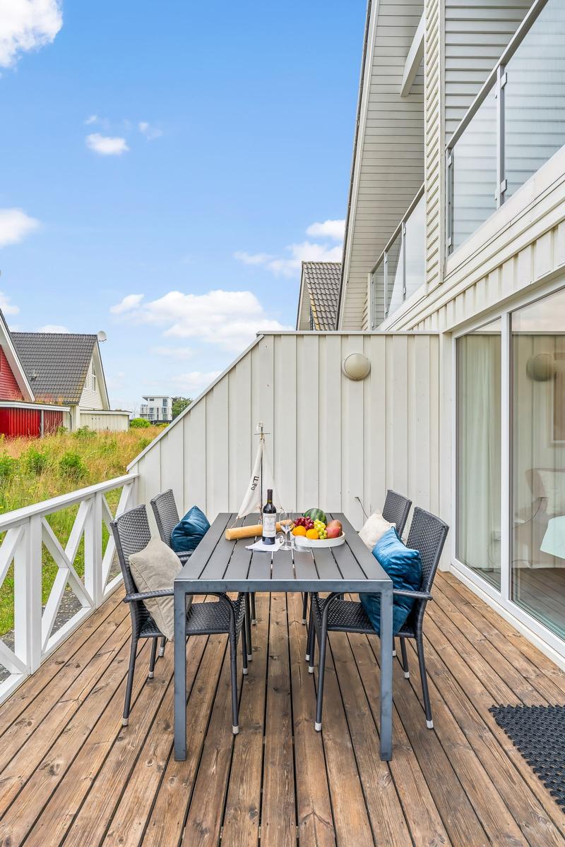 Terrasse mit Tisch und Stühlen, Obst und Wein. Holzdecke, weißer Zaun, Sicht auf Haus und Himmel.