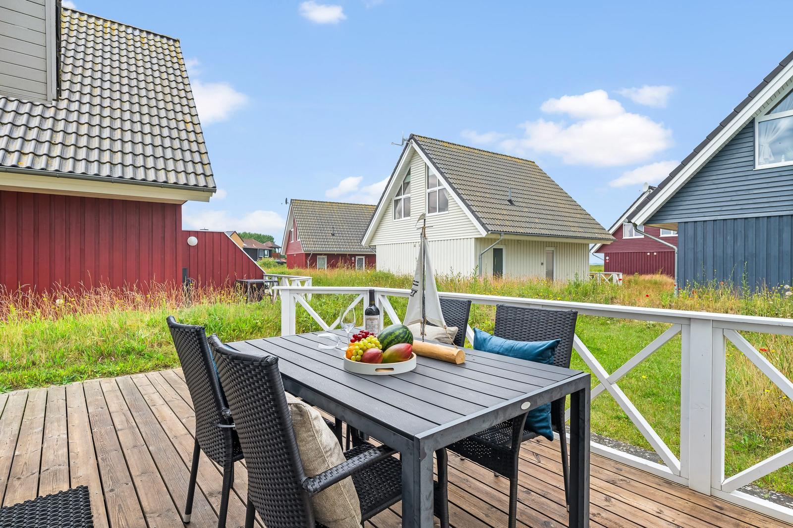Terrasse mit Tisch und Stühlen. Hintergrund: mehrere Häuser und Gras.