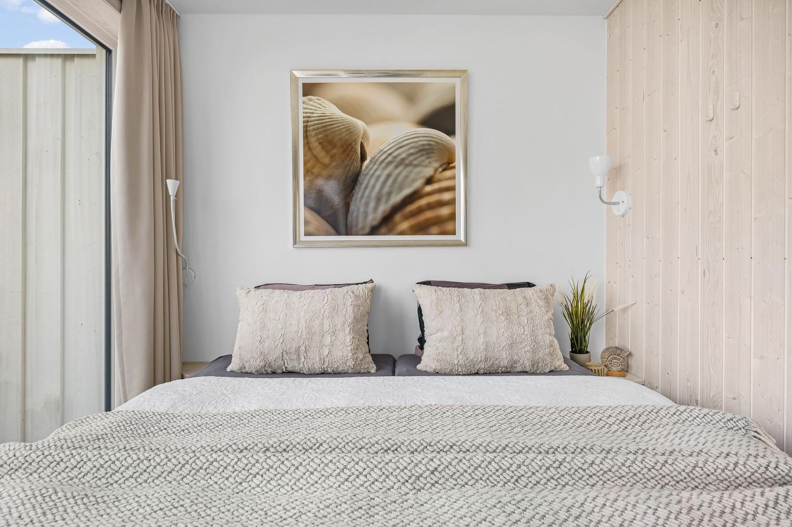 Schlafzimmer mit Bett, Wandbild und Holzwand. Fenster mit Vorhängen.