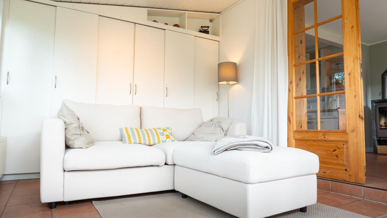 Weißes Sofa mit Kissen und Decke. Hintergrund: weiße Schrankwand und Holztür.