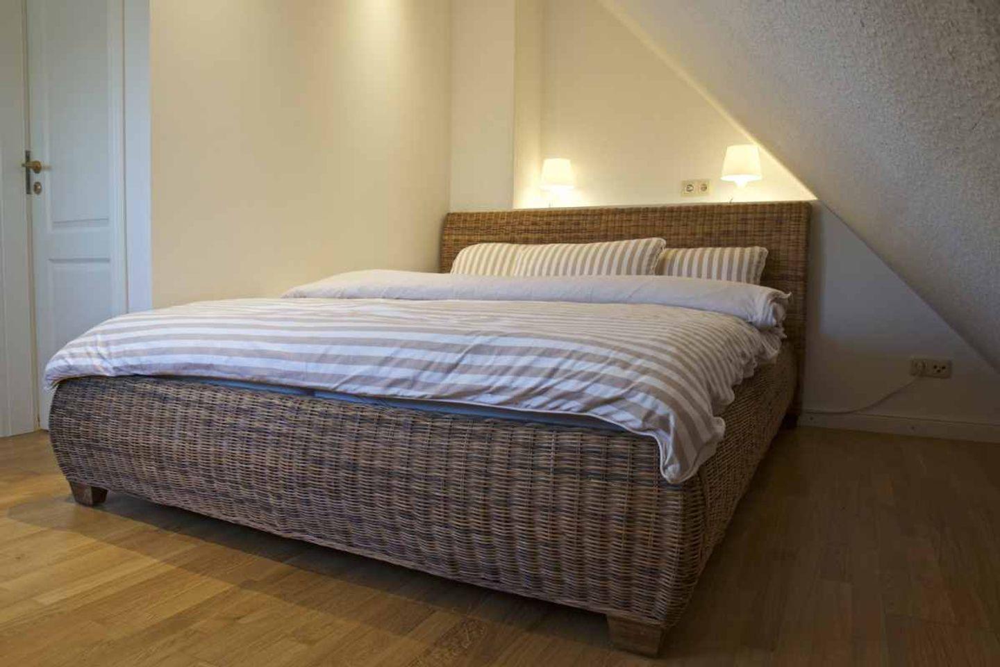 Schlafzimmer mit geflochtenem Bett und Holzboden unter schräger Decke.