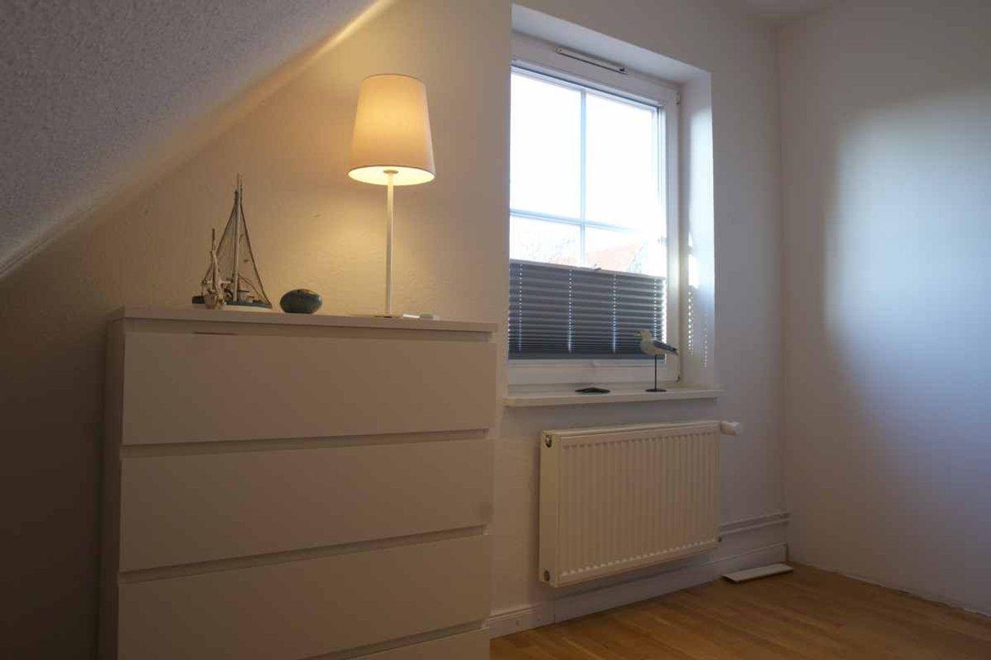 Schlafzimmer mit Schrank, Lampe und Fenster mit Jalousie.