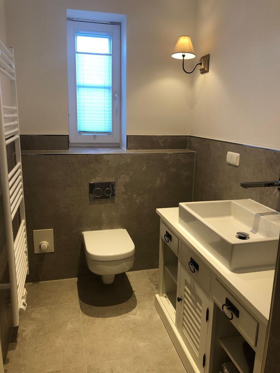 Badezimmer mit Toilette, Waschbecken und Fenster mit Jalousie.
