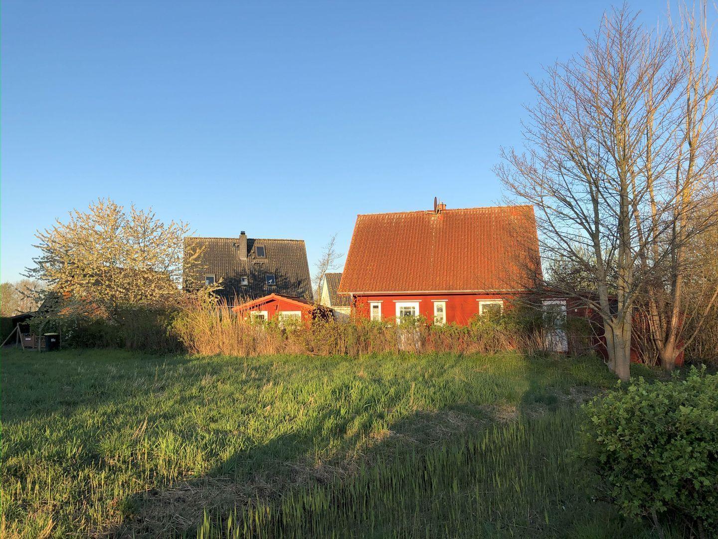 Rotes Haus mit braunem Dach und grünem Grundstück im Freien.