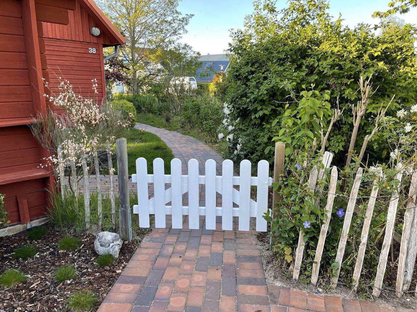Ein gepflasterter Weg führt durch einen Garten mit einem weißen Zaun und Pflanzen.