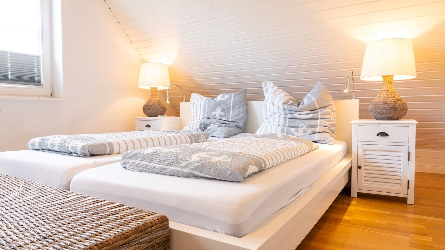Zimmer mit Doppelbett, zwei Nachttischen und Holzboden. An der Wand sind weiße Schieferplatten angebracht.