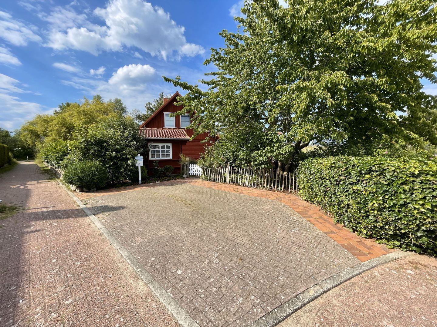 Rotes Haus mit weißen Fenstern, umgeben von Grün und einem gepflasterten Weg.