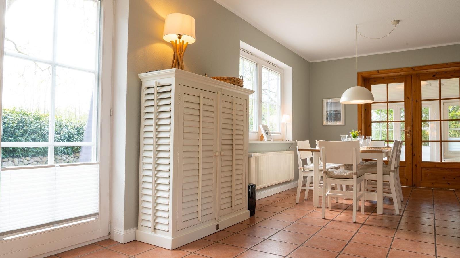Esszimmer mit Holztisch, Stühlen und Fenstern. Weiße Schiebetüren und Terrakottboden.
