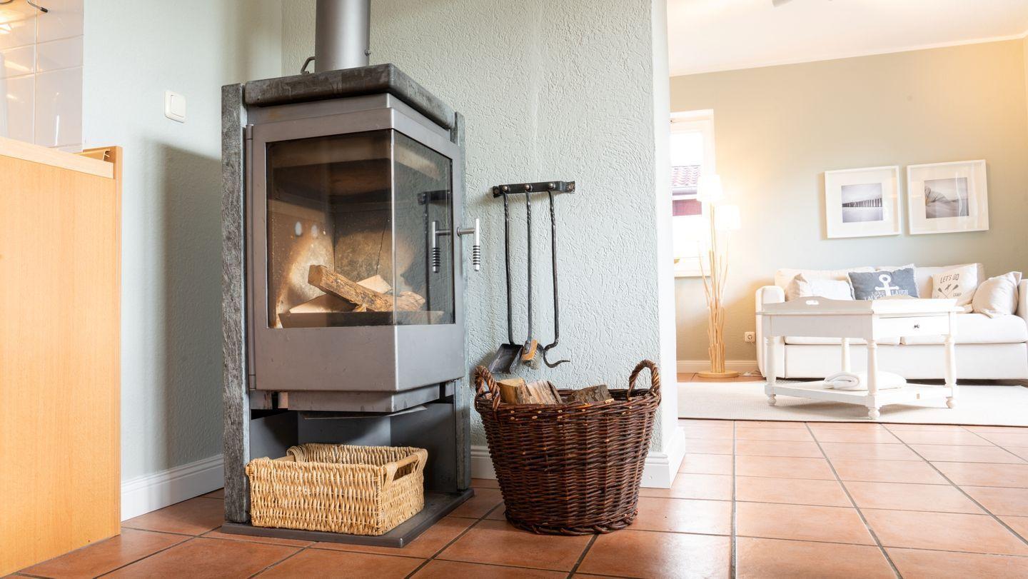 Kaminofen mit Holzstapel und Korb neben Wohnzimmer mit Sofa und Couchtisch.