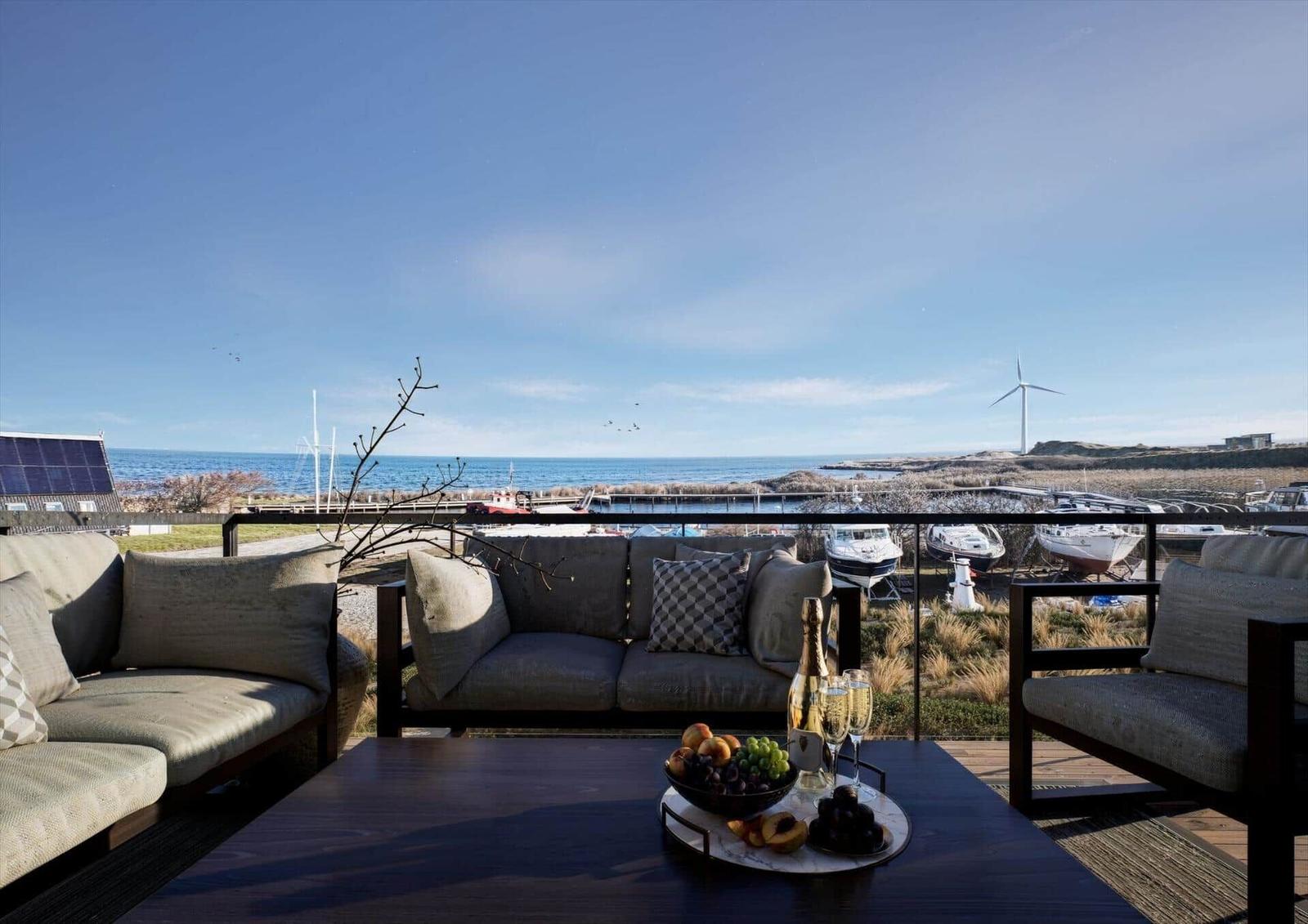 Terrasse mit Sofa und Tisch. Blick auf Meer, Boote und Windkraftanlage.