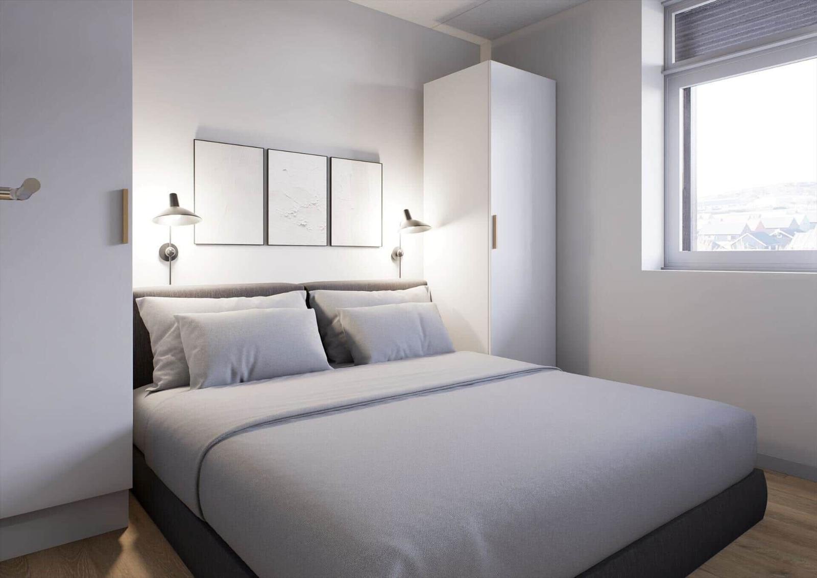 Schlafzimmer mit Bett, Kleiderschrank und Fenster. An der Wand hängen drei Bilder.