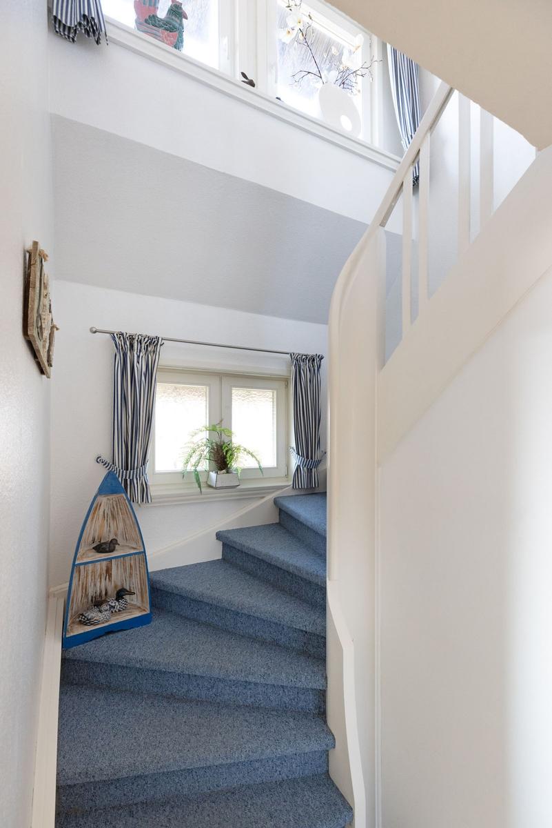 Treppe mit blauem Teppich führt zu einem Fenster mit Streifen-Vorhängen.