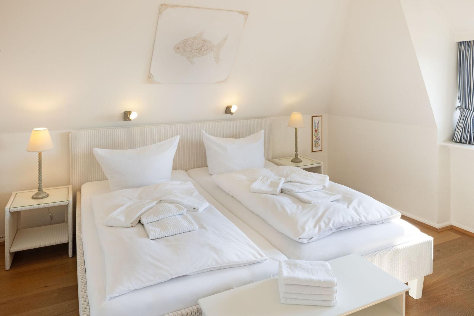 Zwei Betten mit weißen Laken und Handtüchern. An der Wand hängt ein Fischbild.
