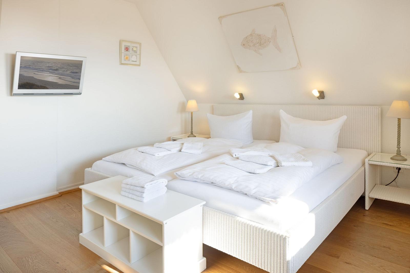 Schlafzimmer mit Doppelbett, weißen Bettwäsche und Holzboden.