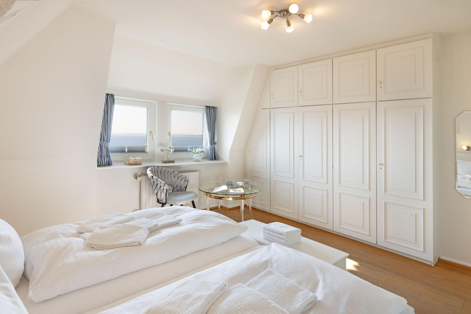 Schlafzimmer mit Doppelbett, weißen Schränken und Fenster mit Meerblick.