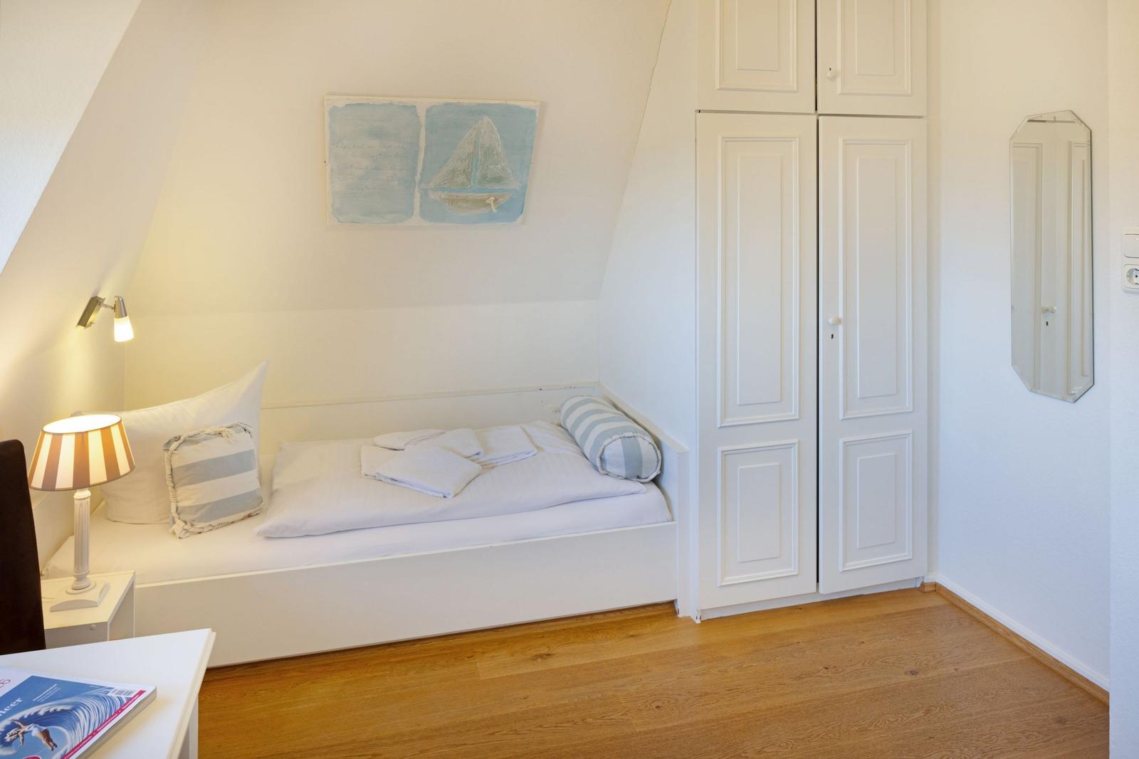 Schlafzimmer mit Bett, Kleiderschrank und Wandbild mit Segelboot.