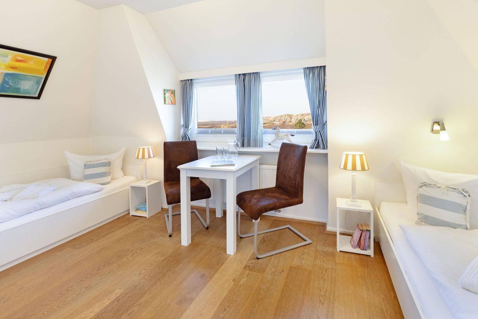 Zimmer mit zwei Betten, Tisch und Stühlen, Fenster mit Blick.