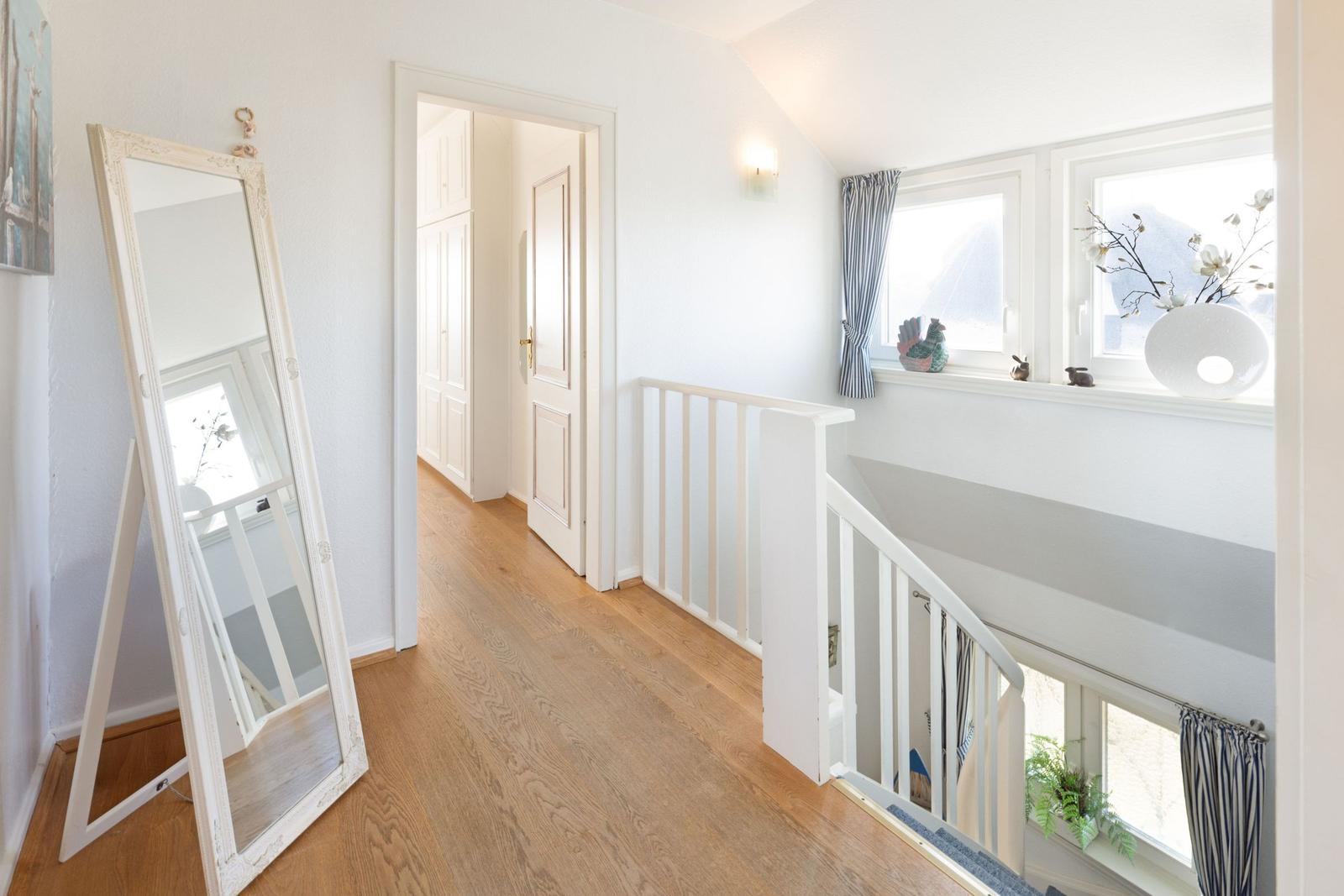 Hausflur mit Holzboden, Spiegel und Treppe zur oberen Etage.