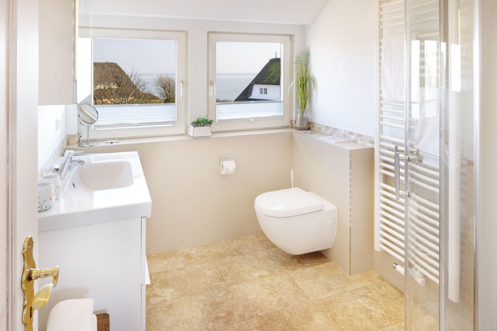 Badezimmer mit Dusche, Toilette und Waschbecken. Fenster mit Meerblick.