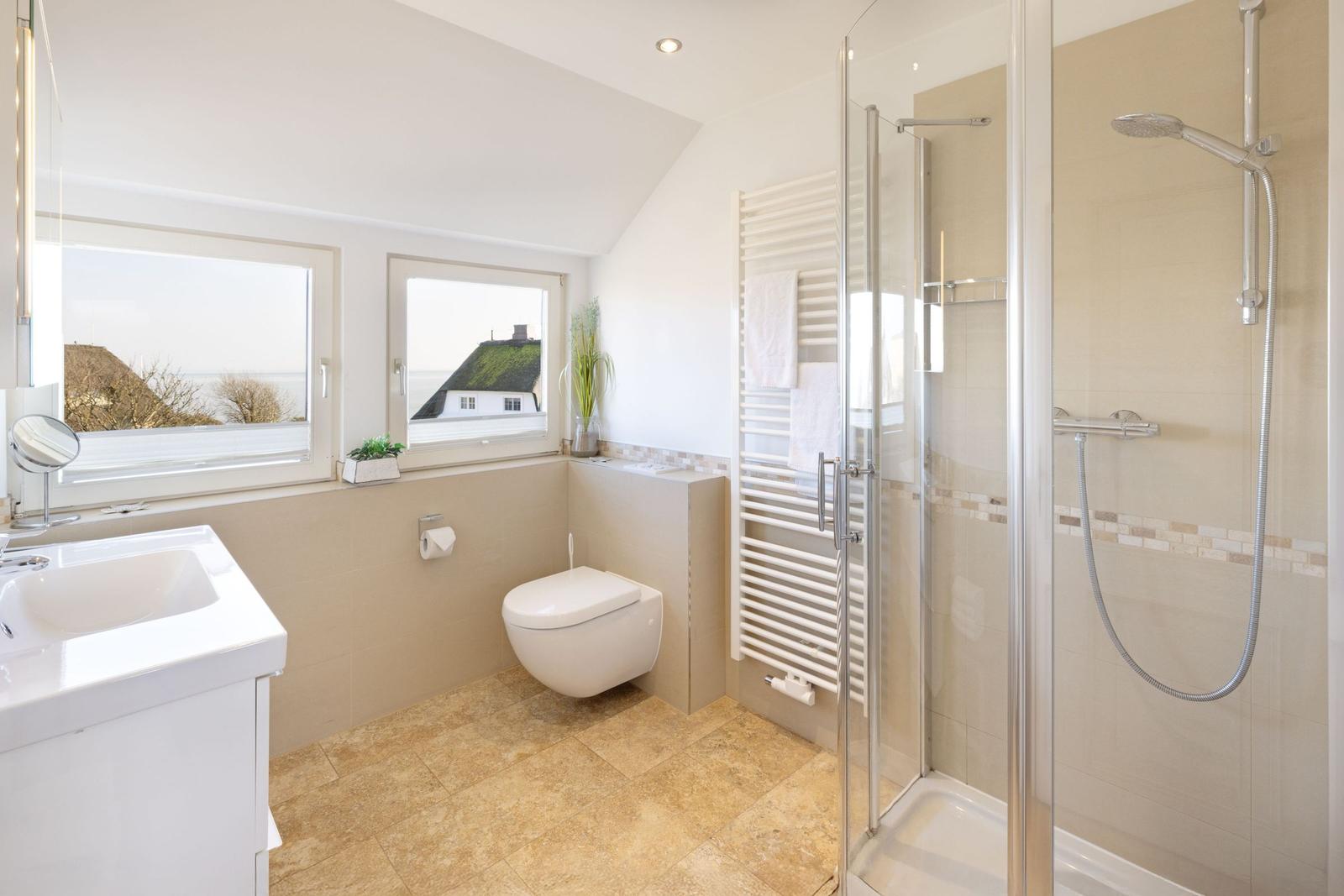 Badezimmer mit Dusche, Toilette und Waschbecken. Fenster mit Blick auf Haus und Meer.