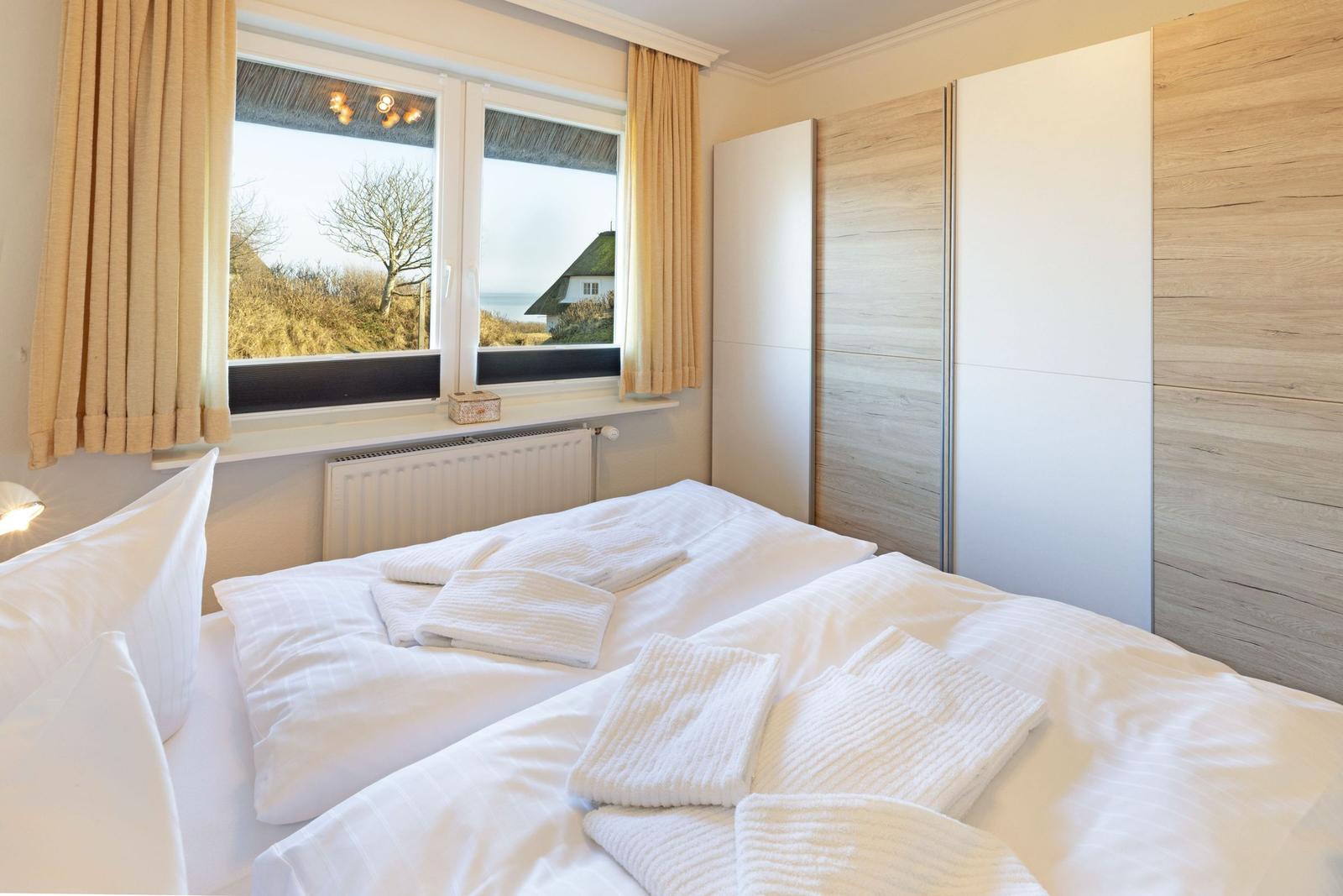 Schlafzimmer mit Bett, Kleiderschrank und Fensterblick auf Landschaft.