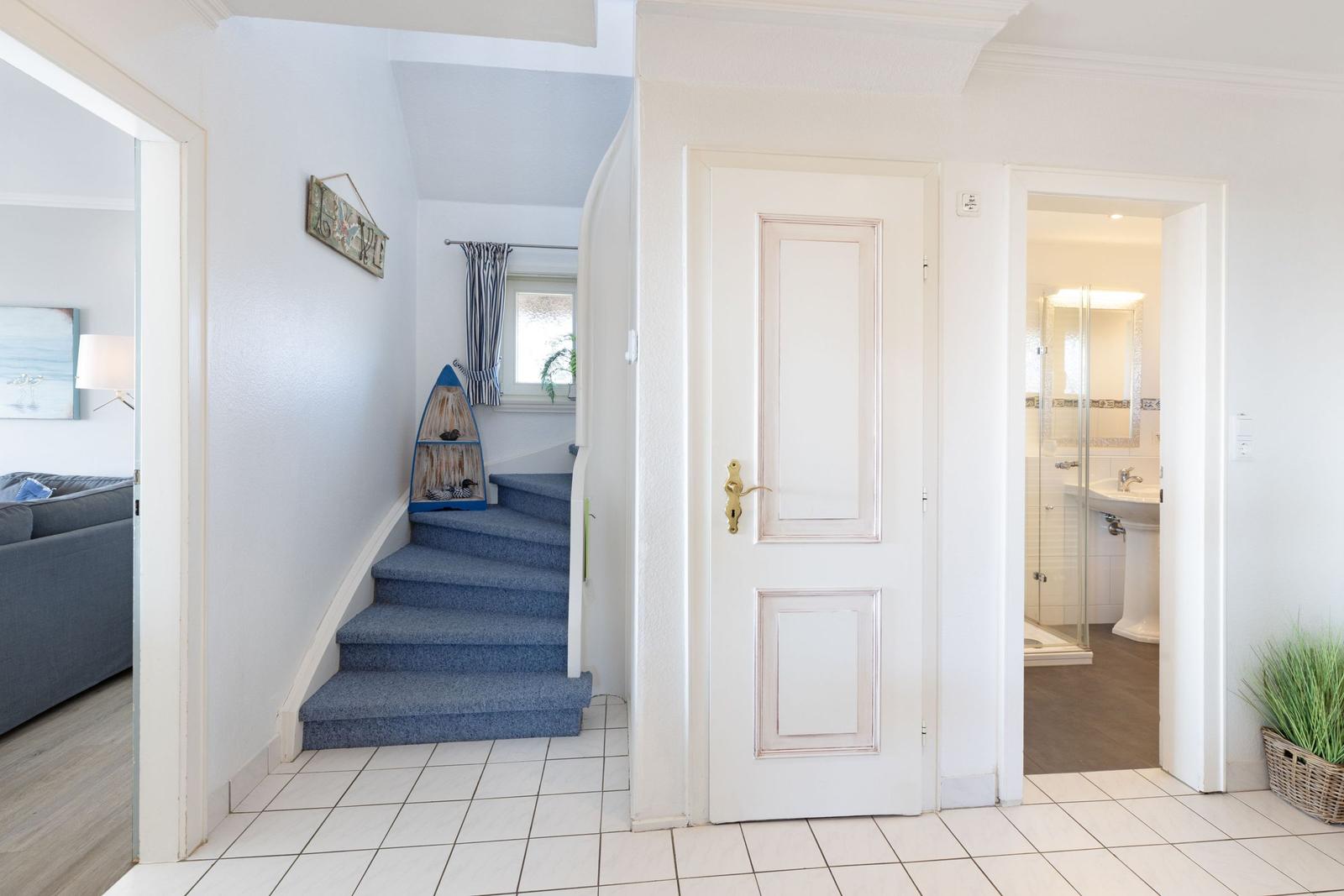Eingangsbereich mit Treppe, Tür und Blick in Bad und Wohnzimmer.