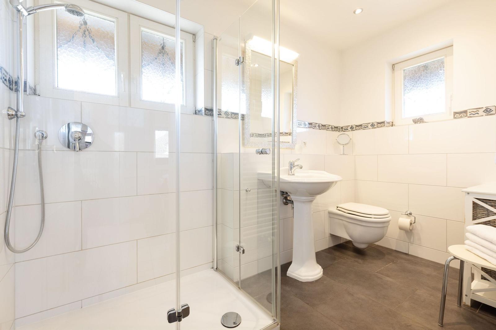 Bad mit Dusche, Waschbecken und Toilette. Fenster mit getöntem Glas.
