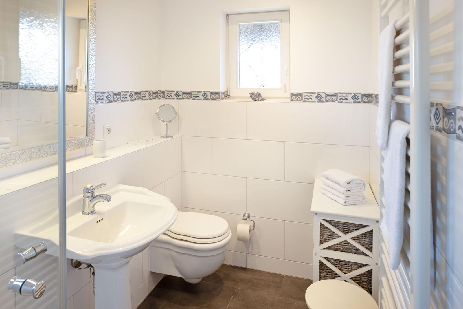 Badezimmer mit Waschbecken, Toilette und Heizung. Fenster und Handtuchhalter sichtbar.
