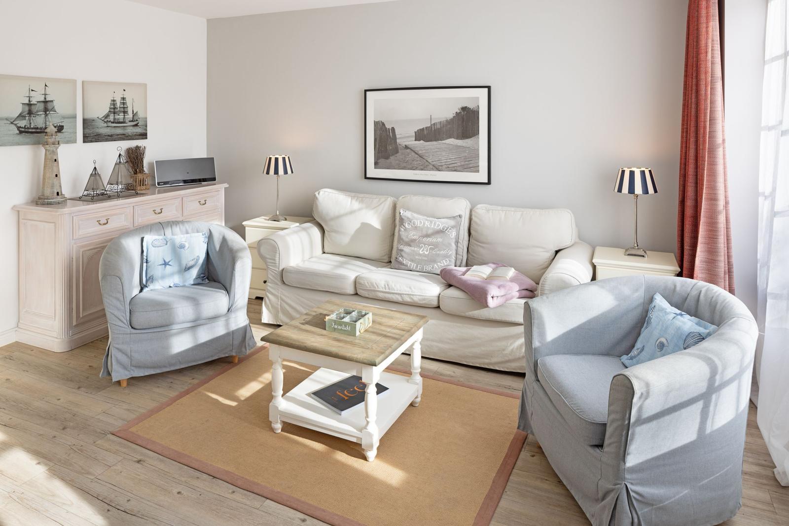 Wohnzimmer mit Sofa, zwei Sesseln, Couchtisch und Wandbildern.