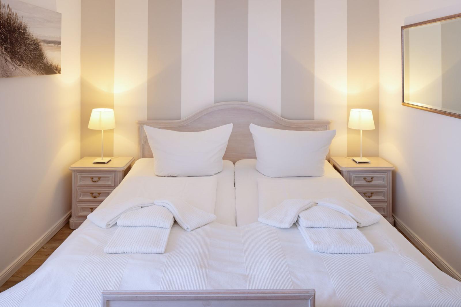 Schlafzimmer mit Bett, zwei Nachttischen und Lampen. Wandtapete mit Streifenmuster.