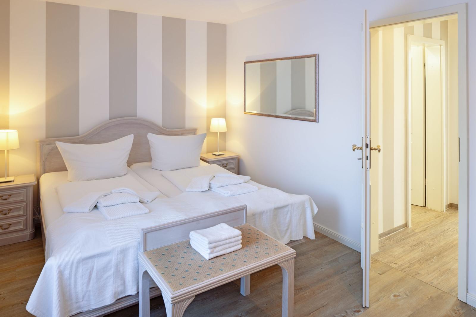 Schlafzimmer mit Doppelbett, Nachttischen und Spiegel. Tür führt in angrenzenden Raum.