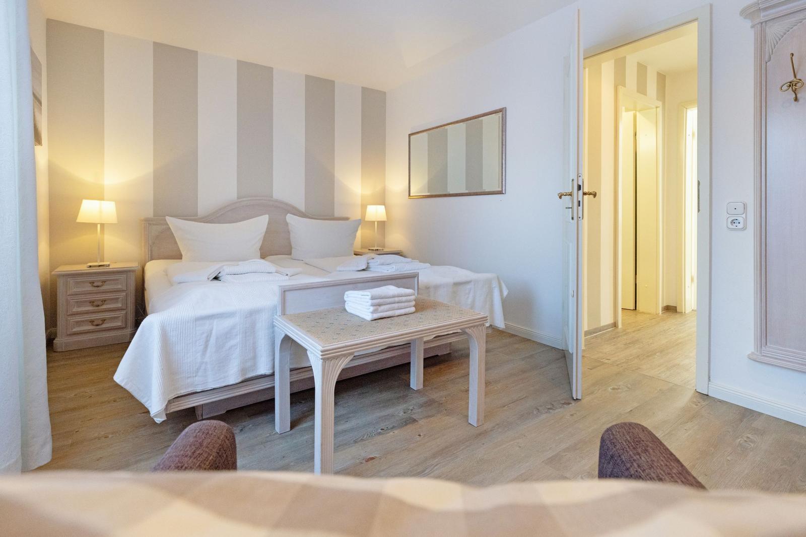 Schlafzimmer mit Bett, Nachttischen und Spiegel an der Wand. Holzfußboden und Tür zum Flur.