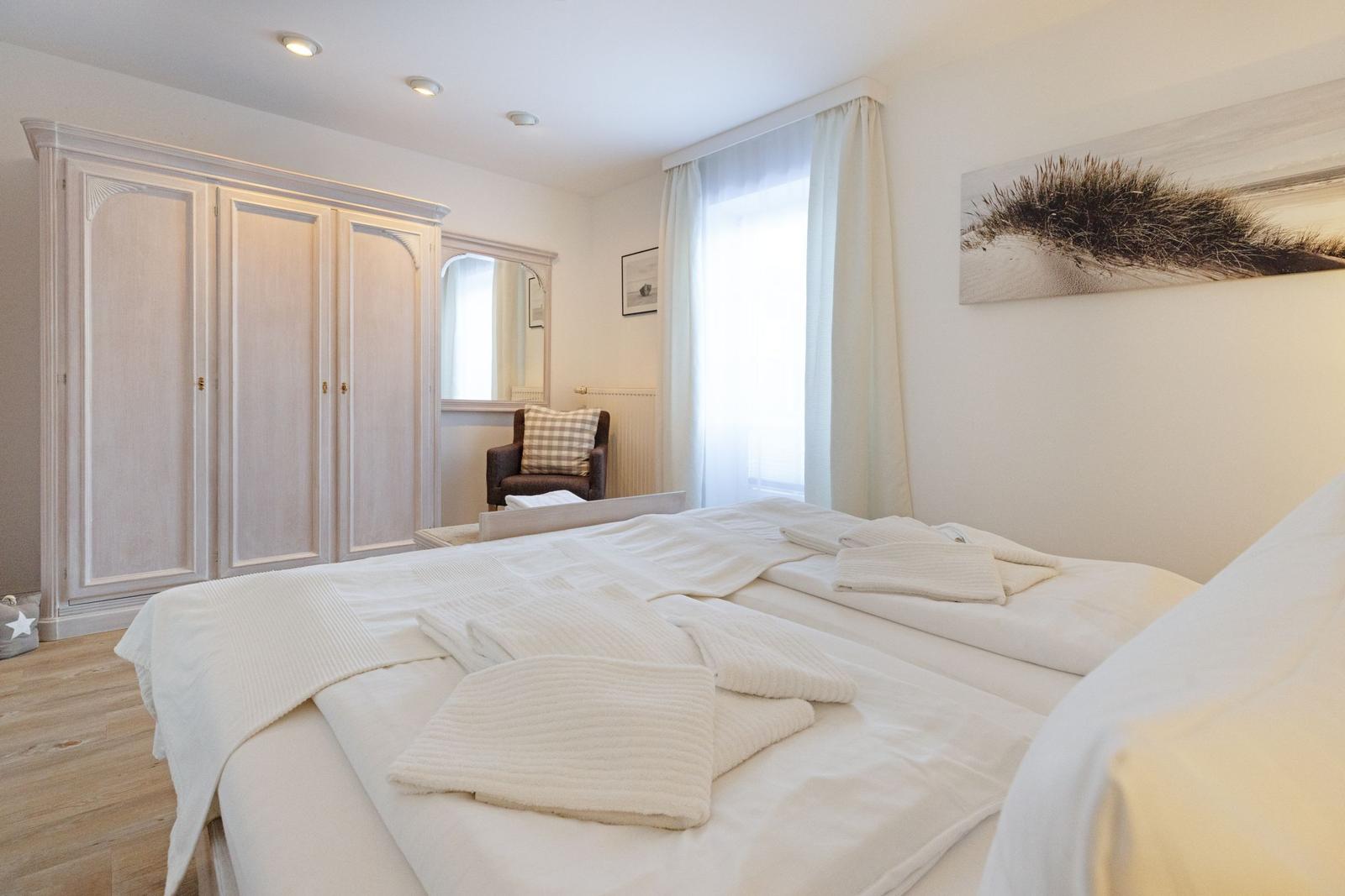Schlafzimmer mit großem Bett, Kleiderschrank und Fenster mit Vorhängen.