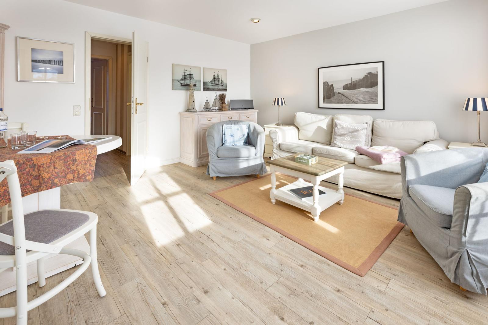 Wohnzimmer mit Sofa, Sessel und Esstisch. Holzboden und Wandbilder.