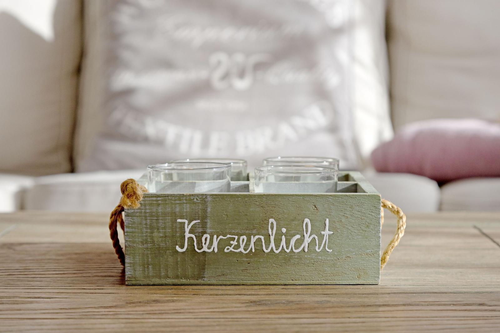 Holztablett mit Kerzenhaltern steht auf Tisch vor Sofa.