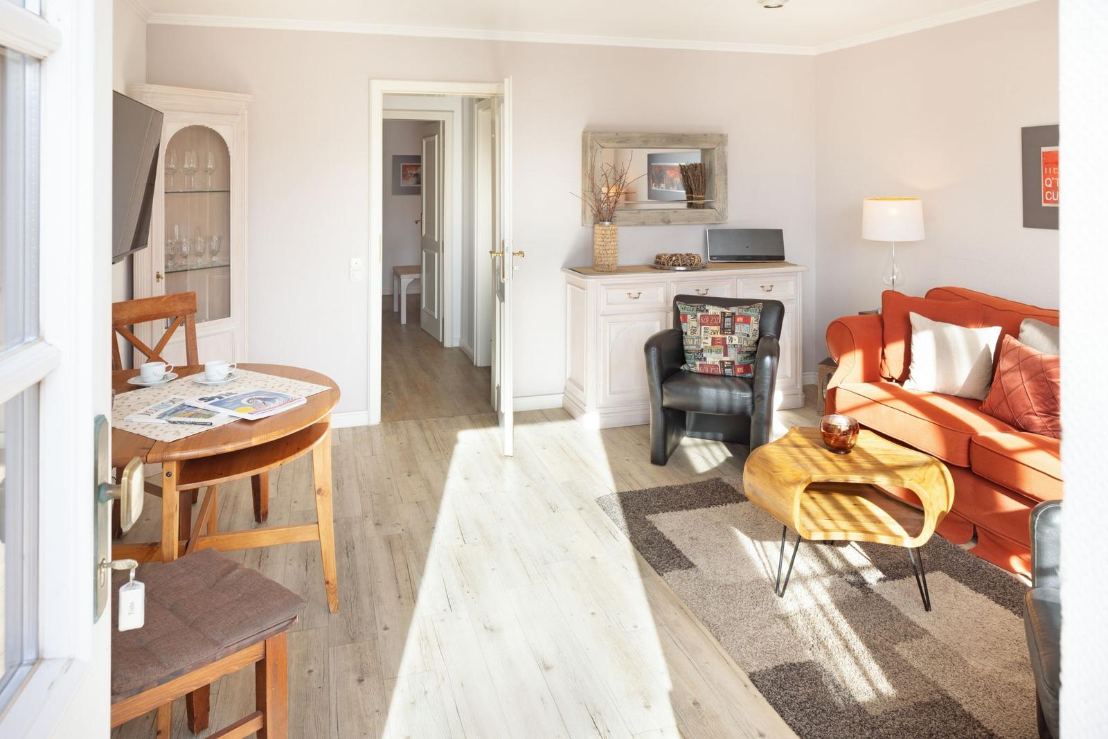 Living and dining area with orange sofa, wooden table, and white furniture.