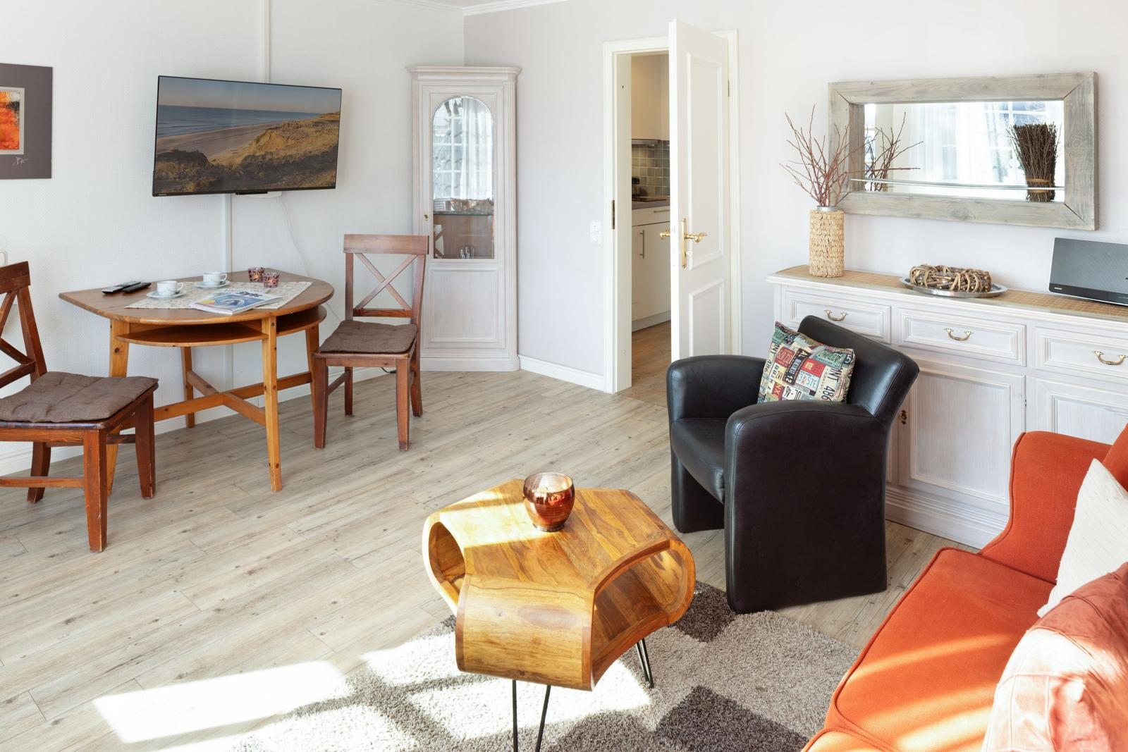 Living room with dining area, sofa, armchair, and TV. Wooden floor and white walls.