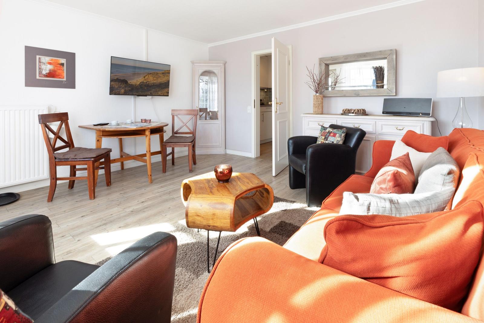 Living room with orange sofa, dining area, and TV. Wooden floor and white walls.