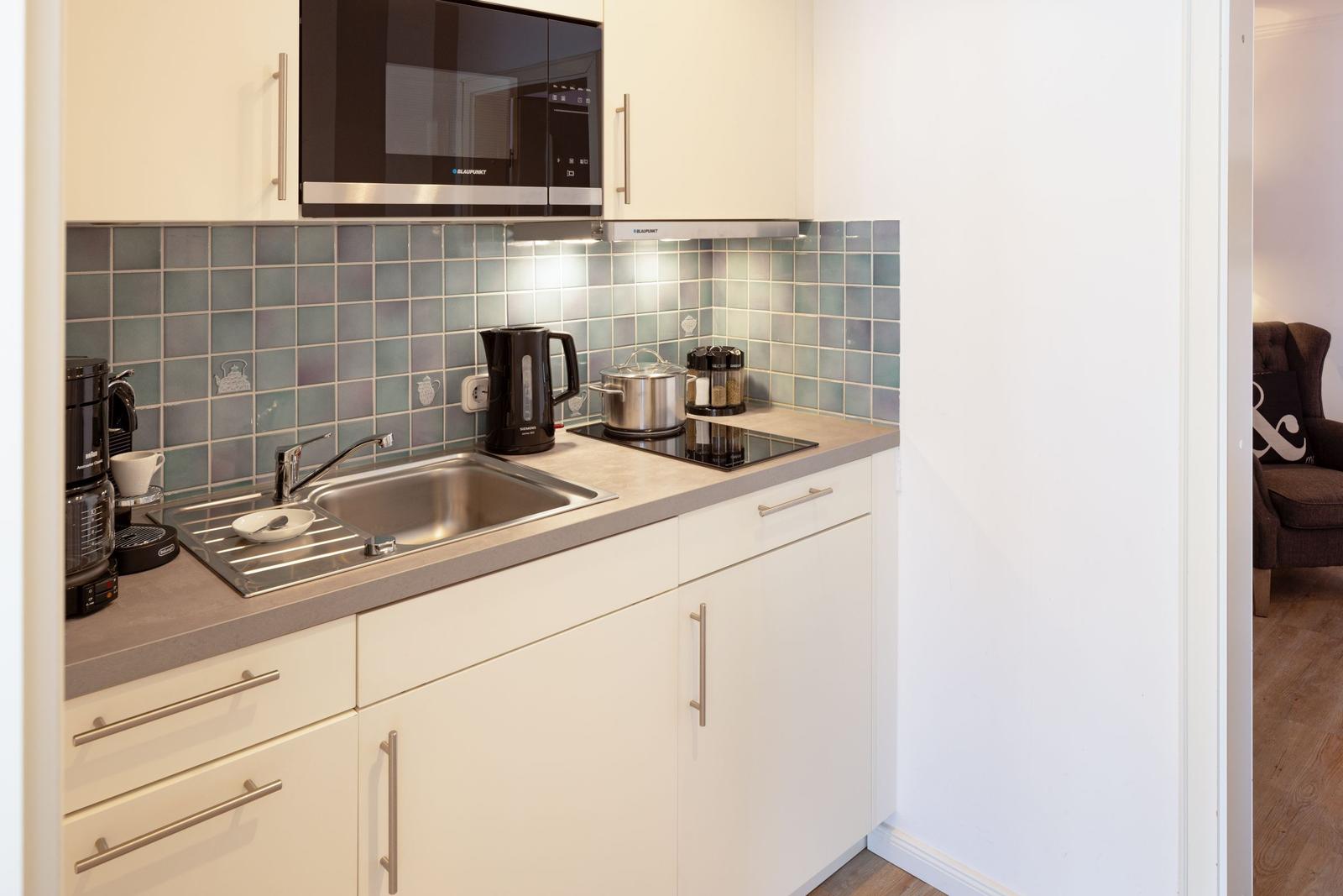 Kitchen with sink, stove, and microwave. Tile backsplash and white cabinets.