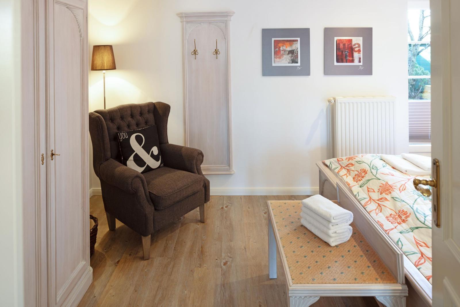 A bedroom with bed, armchair, coat hooks, and window.