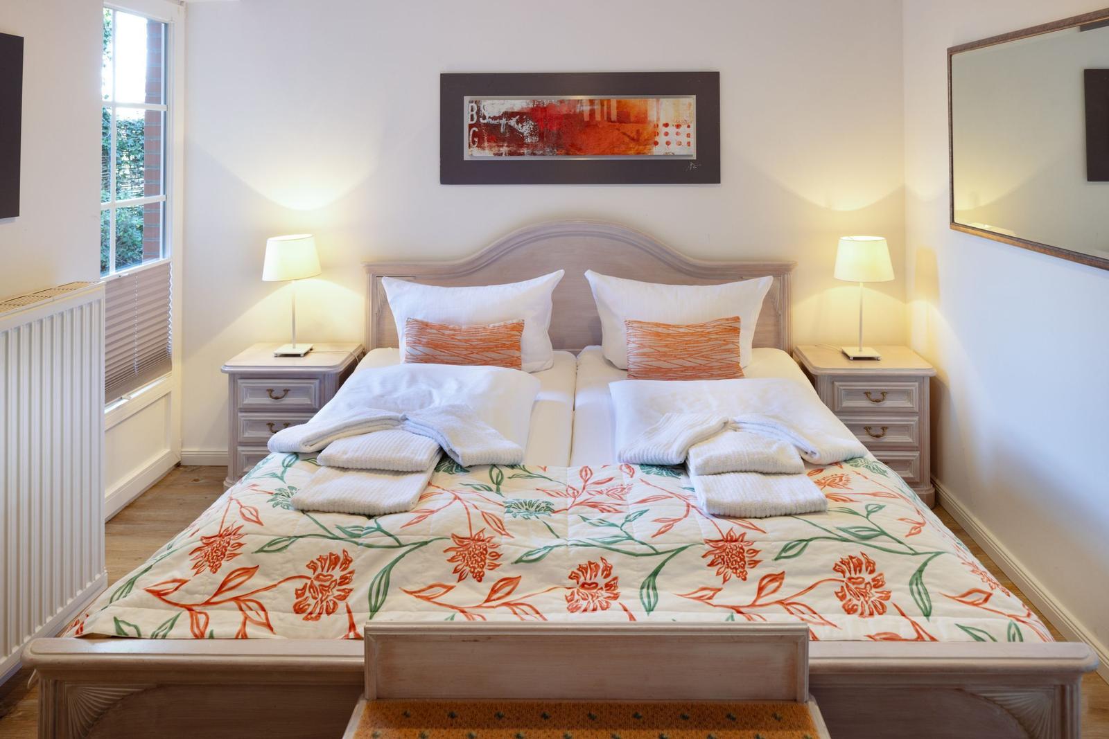 Double bed with patterned bedspread, two nightstands with lamps, and wall art above headboard.