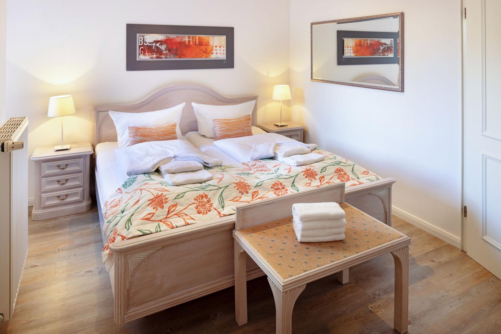 A bedroom with a double bed, two nightstands, a mirror, and wooden floor.