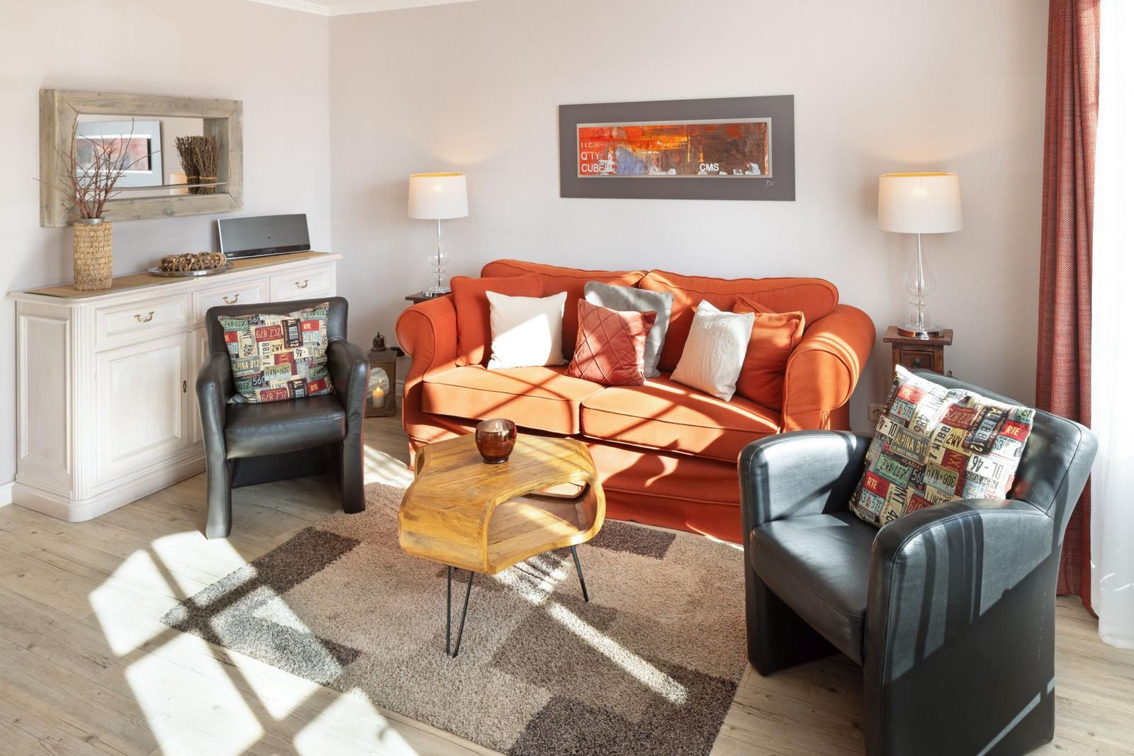 A living room with an orange sofa, two black chairs, and a wooden table.